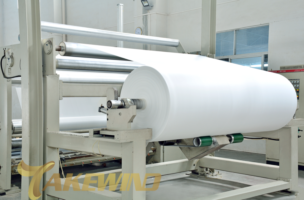 A biodegradable non-woven fabric production line is rapidly producing rolls of white non-woven fabric.