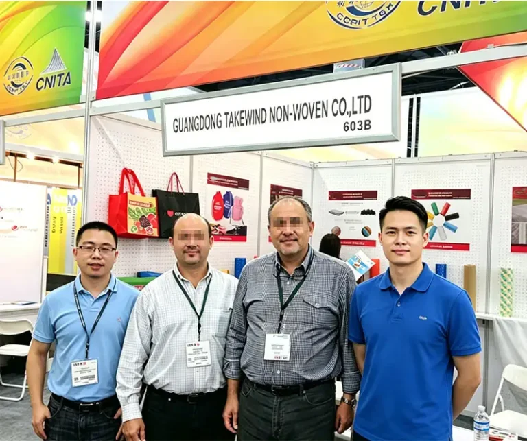Group picture at Guangdong Takewind Non-Woven exhibition booth, two Takewind sales staff taking photos with two furniture manufacturers from Poland after discussing furniture nonwoven fabric cooperation