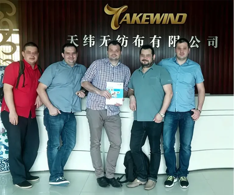 Five purchasing managers from Polish furniture manufacturers take group photo at Takewind Non-Woven front desk after factory inspection, recognizing our furniture-grade nonwoven products