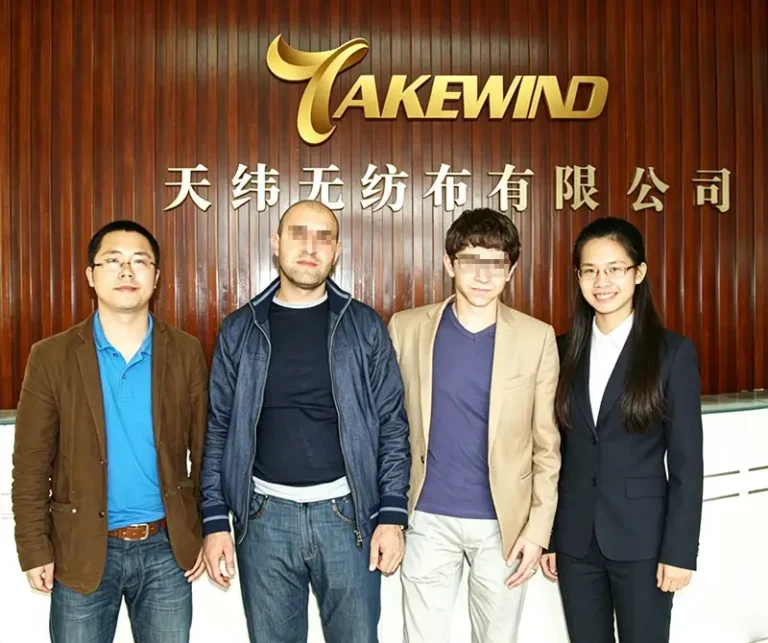 Four people group photo in front of Takewind Non-Woven company reception wall; internal sales staff welcome two Armenian furniture manufacturers for factory inspection and nonwoven bulk order negotiation