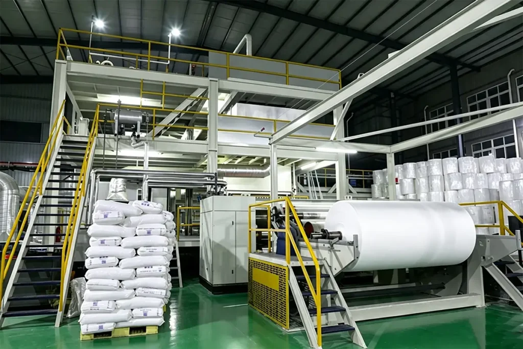 Automatic spunbond production unit with stacked white PP raw material bags and finished white geotextile big rolls