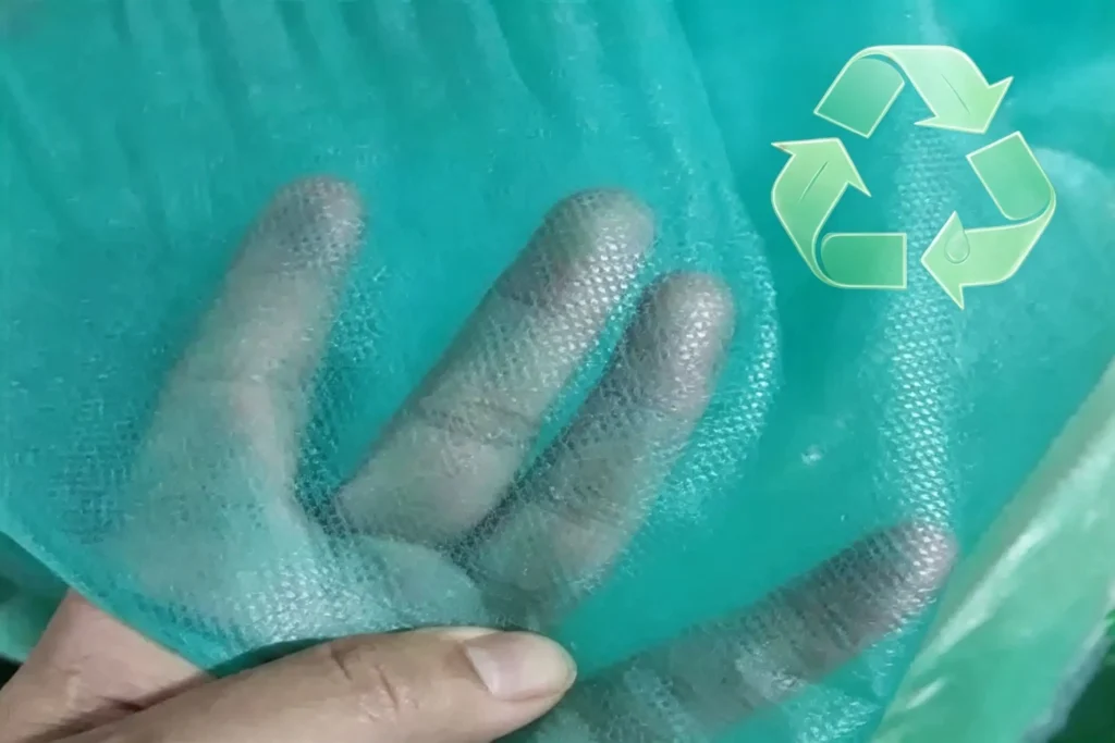 hand penetrates translucent green geotextile with recycle logo, degradable eco nonwoven fabric from Takewind