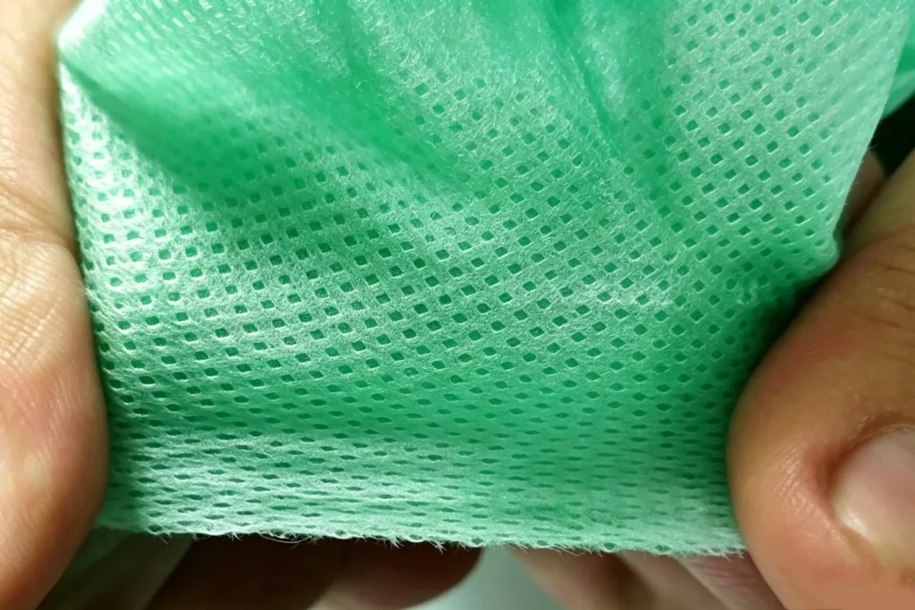 hand stretching green geotextile showing dense mesh structure, tear-resistant spunbond nonwoven fabric