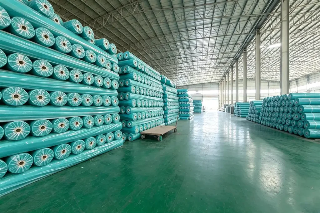 Tidy storage area filled with multiple sizes of green geotextile rolls, matte green warehouse floor for geotextile finished products